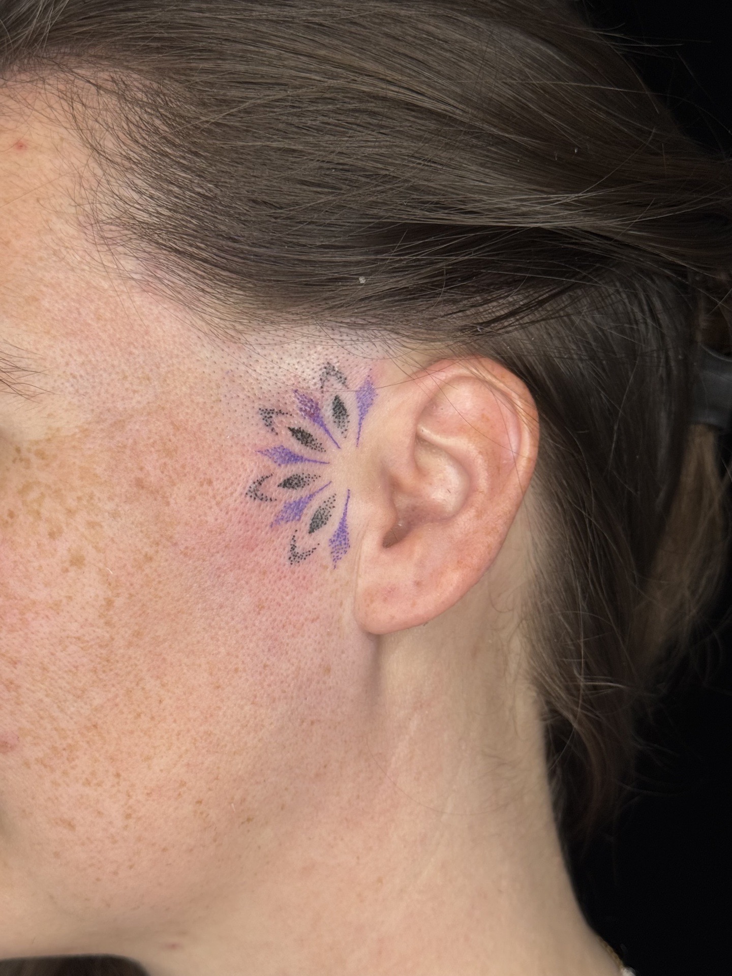 Tatouage mandala coloré près de l’oreille.