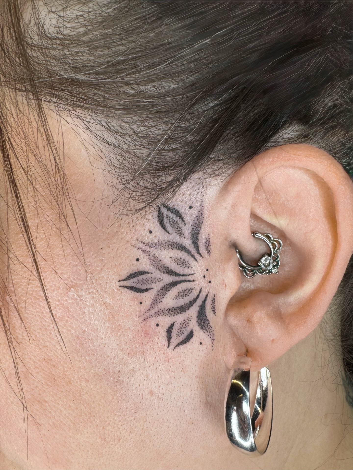 Tatouage mandala noir près de l’oreille.