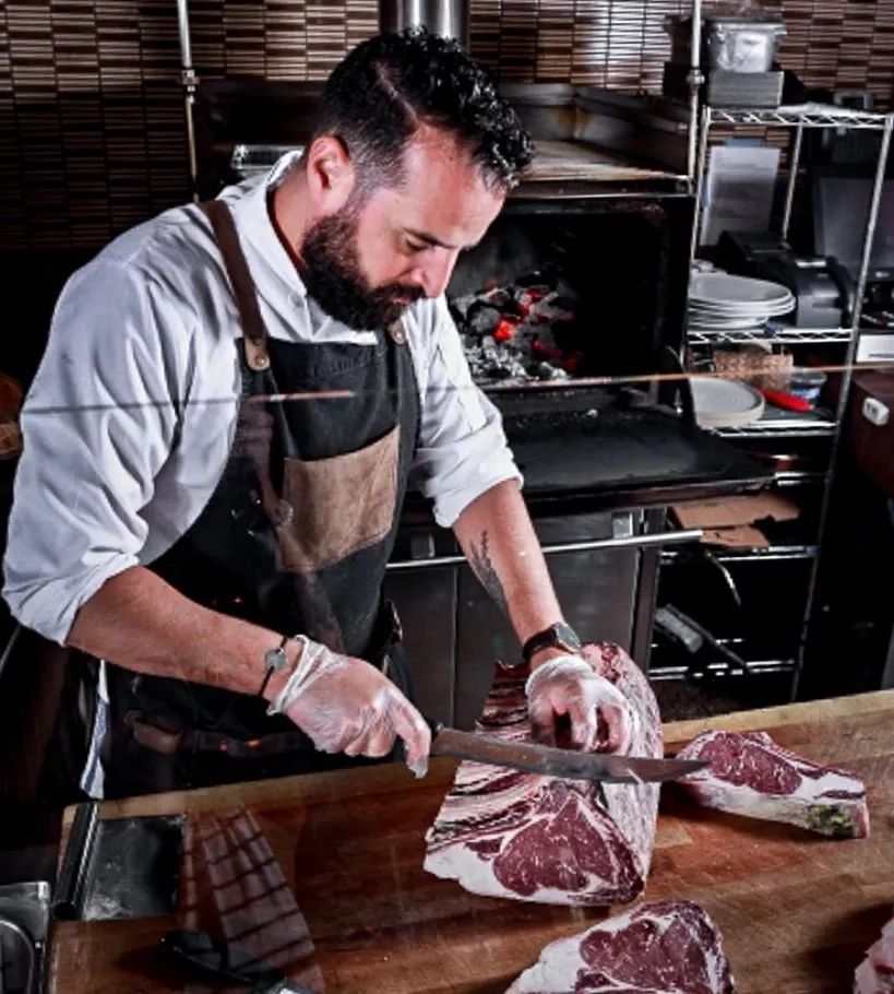 Le chef Abdellah Kamoune tenant deux côtes de bœuf tomahawk devant le feu ouvert