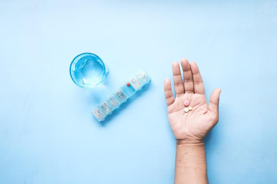 A open palm holding three pills next to a pill box and a glass of water