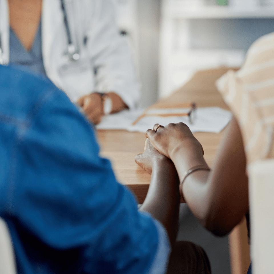 A close up of two people from the back sitting down and holding hands in front of a doctor