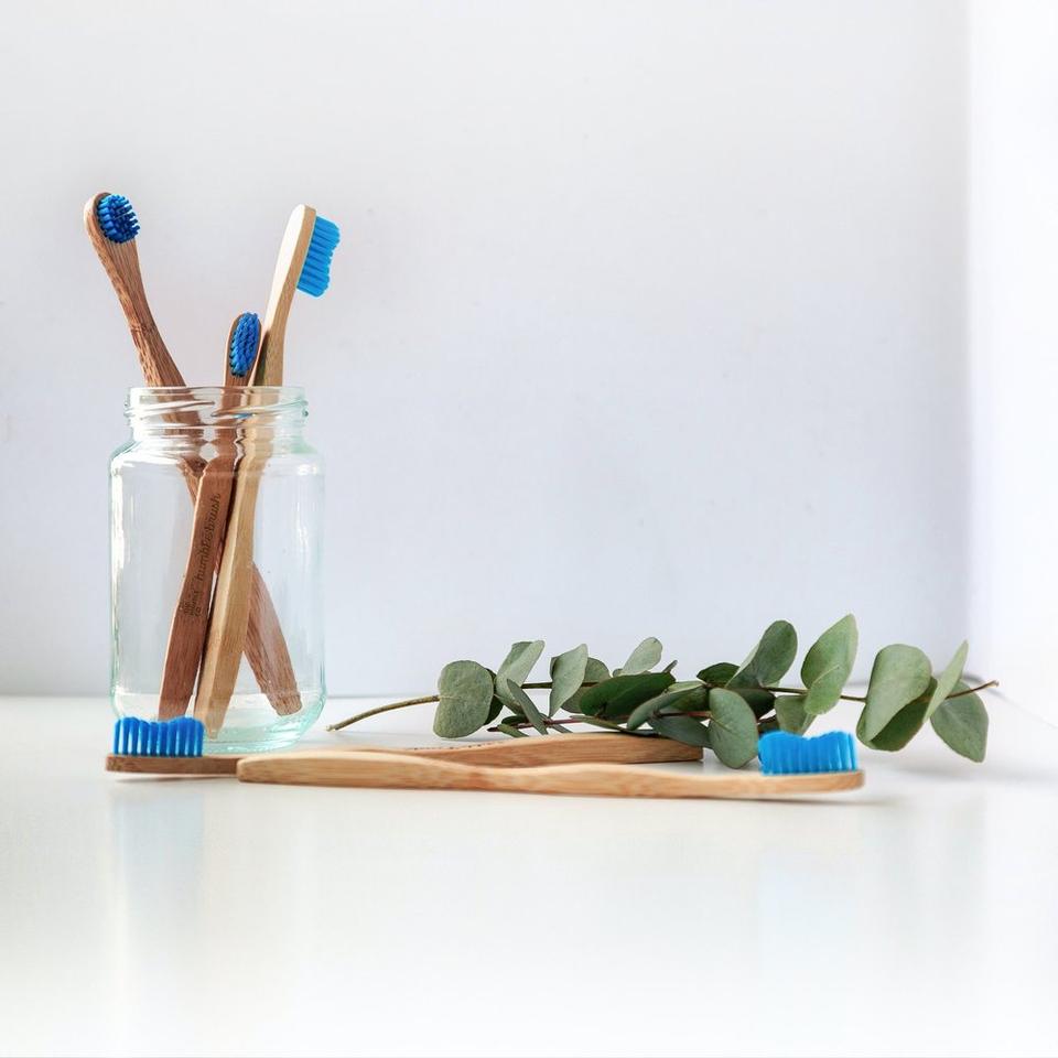 Many bamboo tooothbruses on a counter and in a glass jar