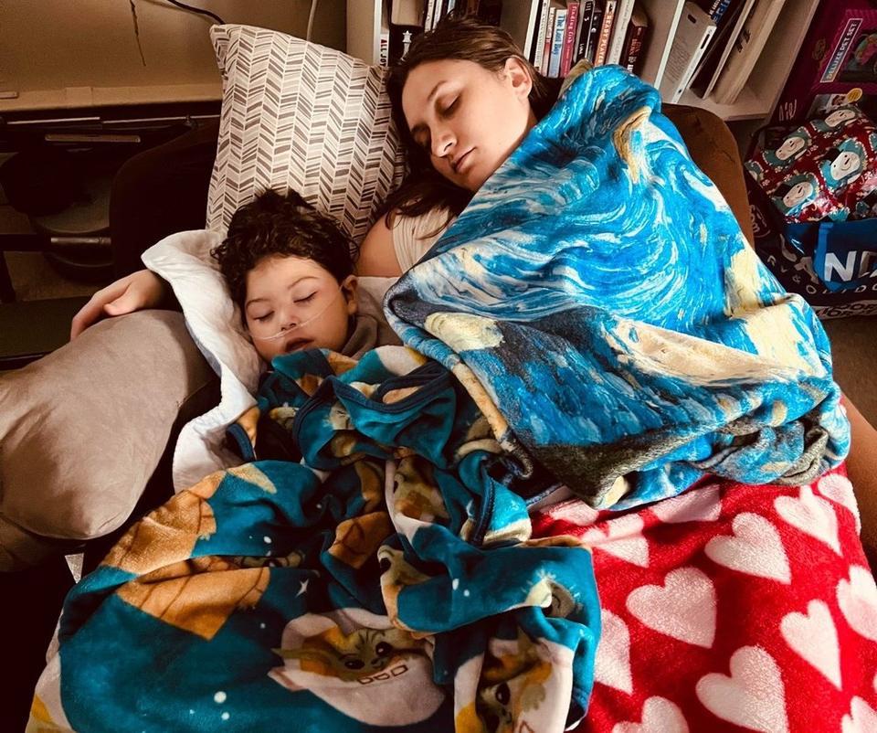 Rare mother Samantha and her medically complex son snuggling and sleeping together on a sofa chair bed under cozy blankets