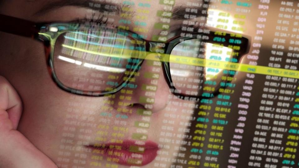 Close-up of a person’s face with glasses, reflecting digital data or code, symbolizing the intersection of technology and analysis.