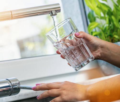 A closeup of hands filling up a glass a water through the water faucet