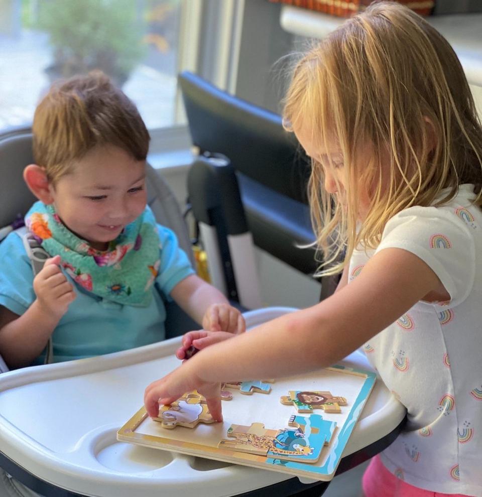 Siblings Hadley (on the left) and Alden with medical complexities in a gait trainer (on the right) playing together.