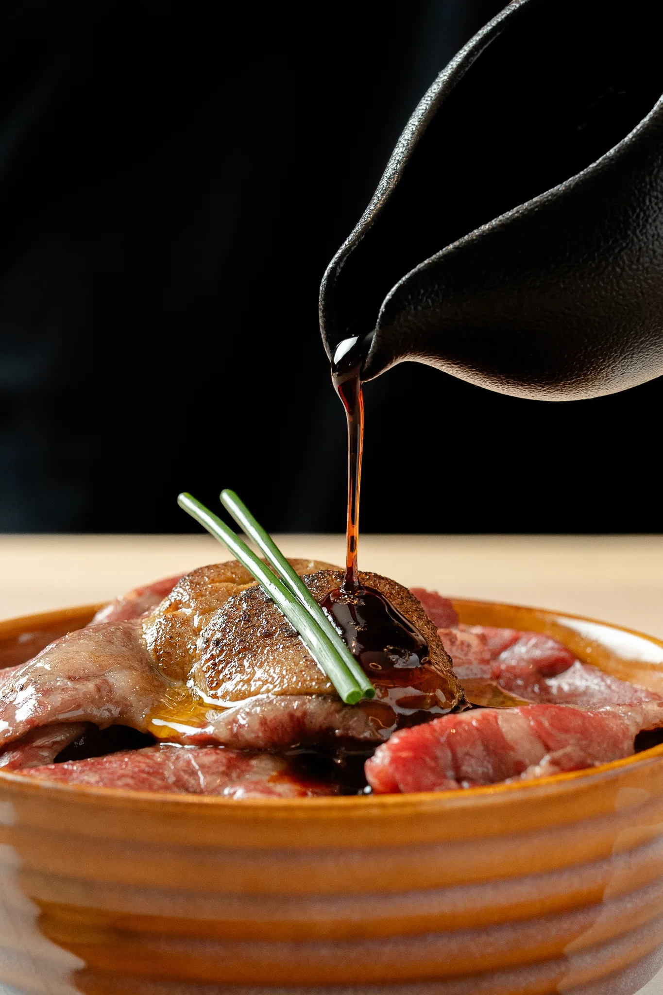 A dark sauce being poured over wagyu and foie gras on rice