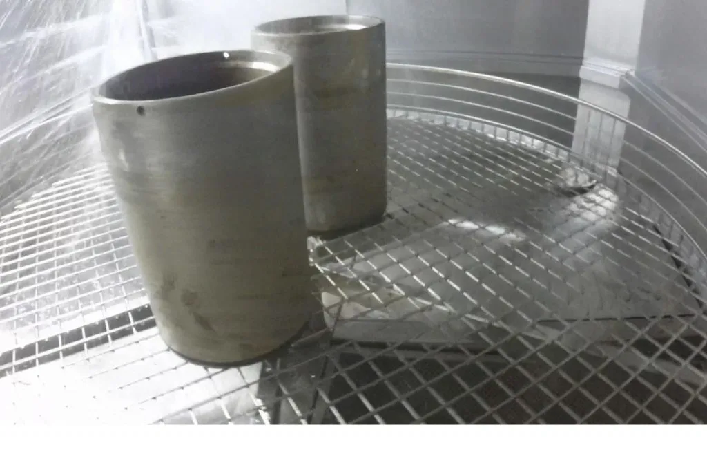 Two machined steel sleeves on the grid in the basket of an automatic parts washer