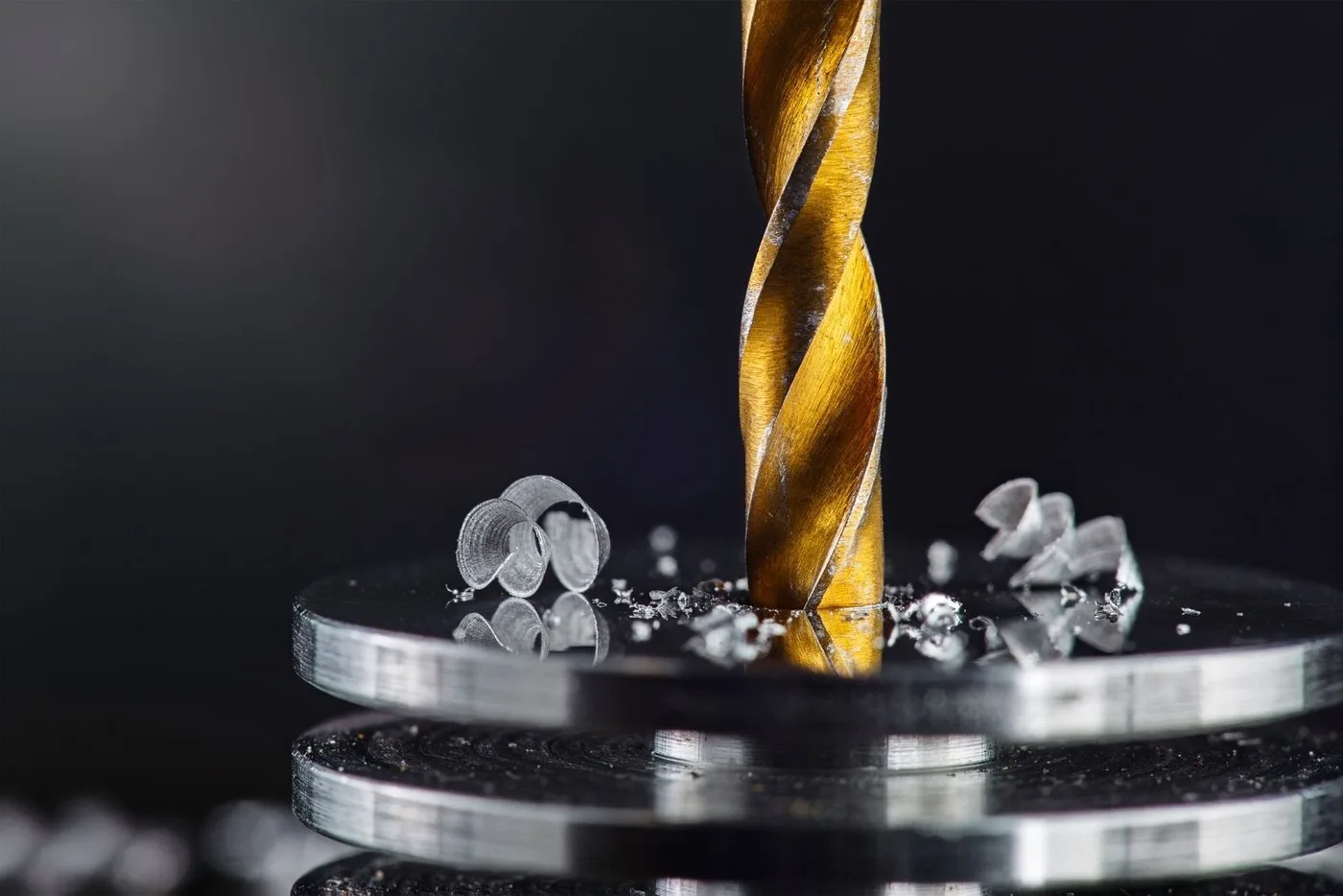 Drill bit in a metal plate with small chips around the hole