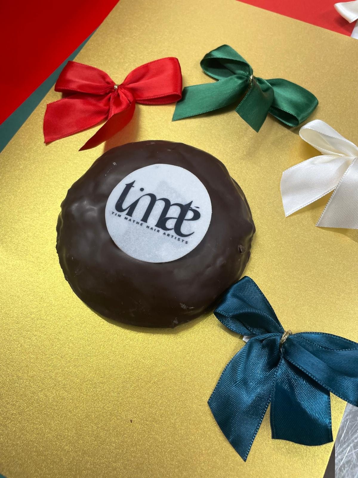 Schokolierter Lebkuchen mit aufgedrucktem Firmenlogo, umgeben von bunten Geschenkschleifen