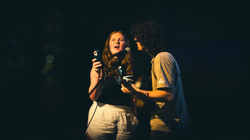 A singer looks upward mid-line while the guitarist beside her plays.