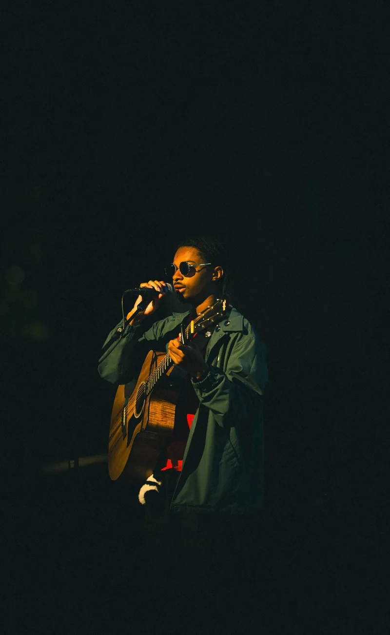 A guitarist singing into the microphone, guitar raised, stage otherwise dark.