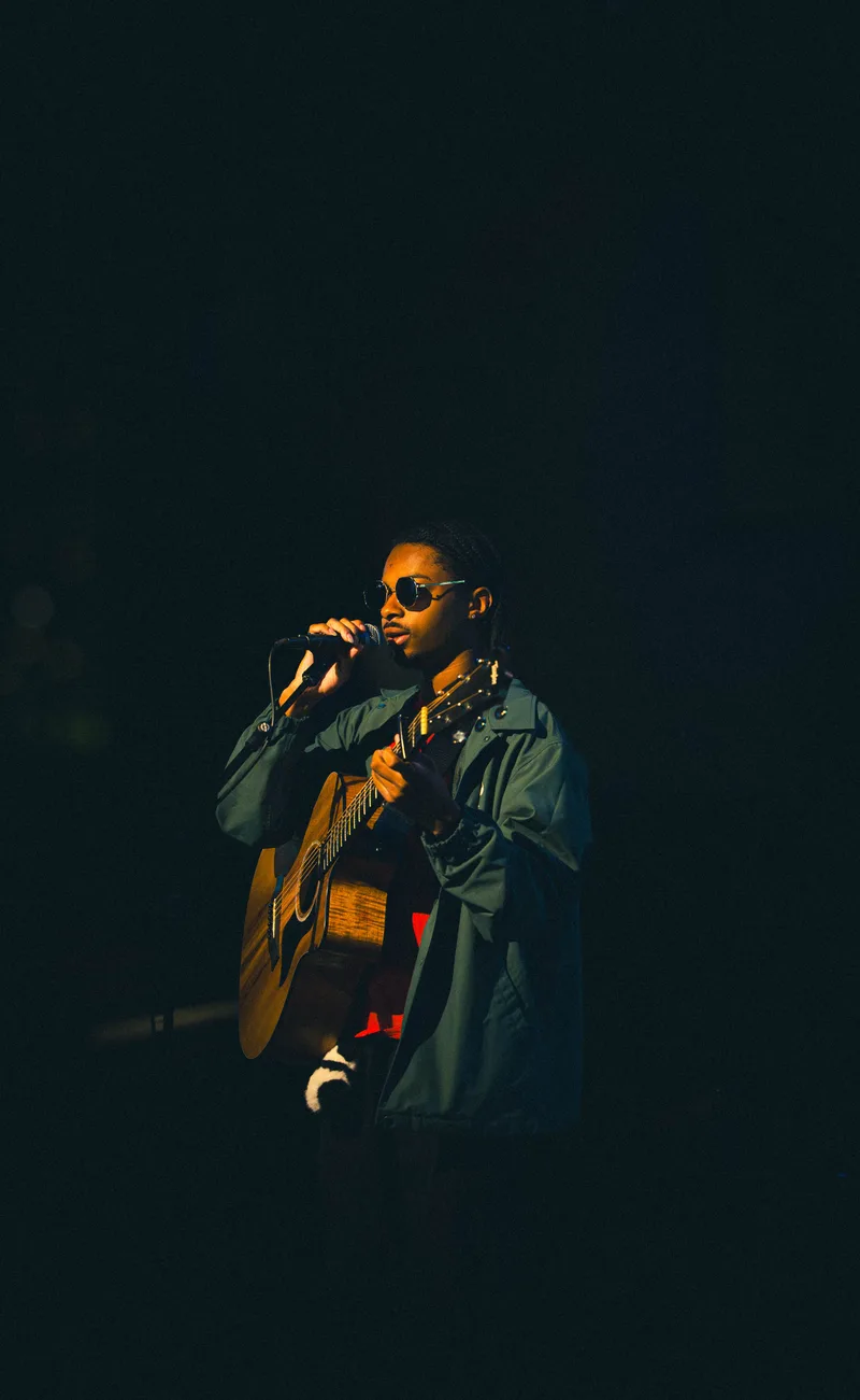 A guitarist in round sunglasses sings into the microphone, guitar held high.
