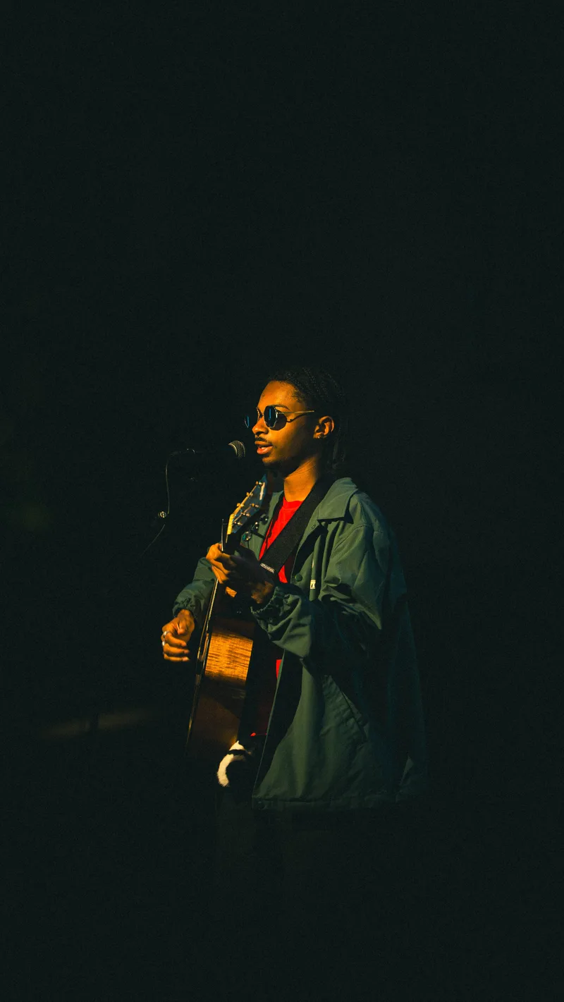 A guitarist at the microphone, green jacket catching the warm stage light.