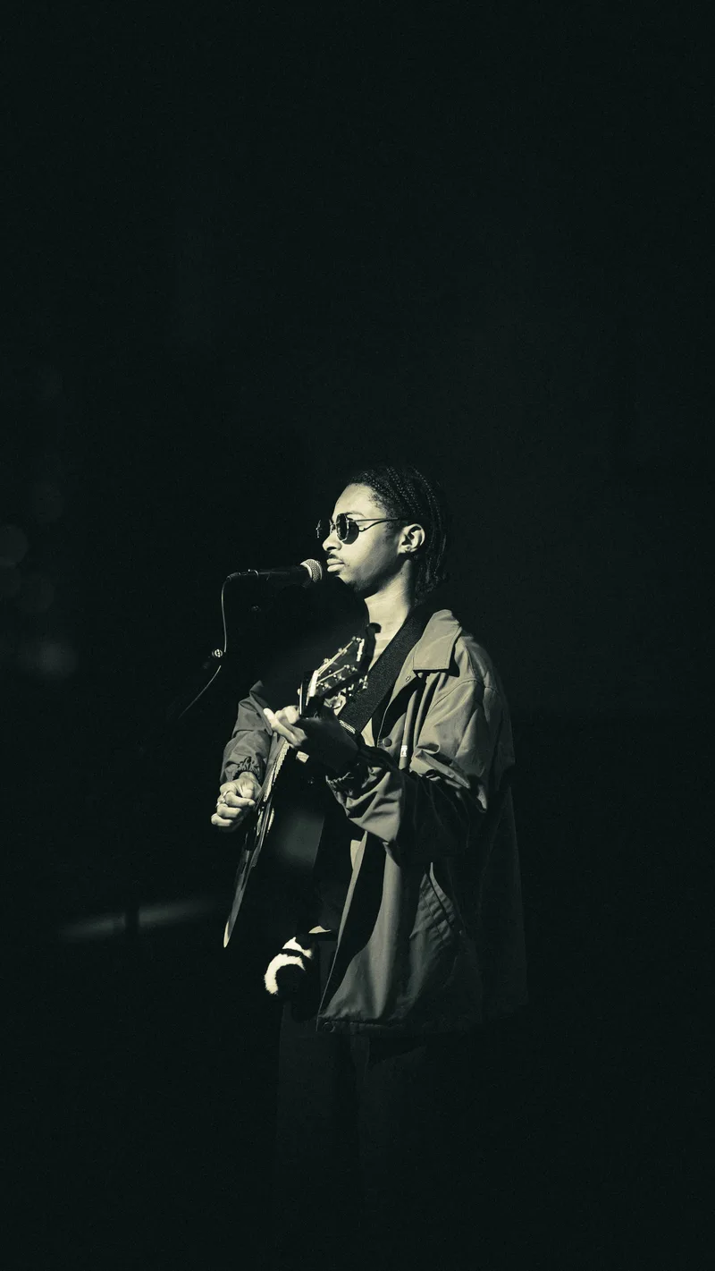 Black and white frame of a guitarist singing into the microphone.
