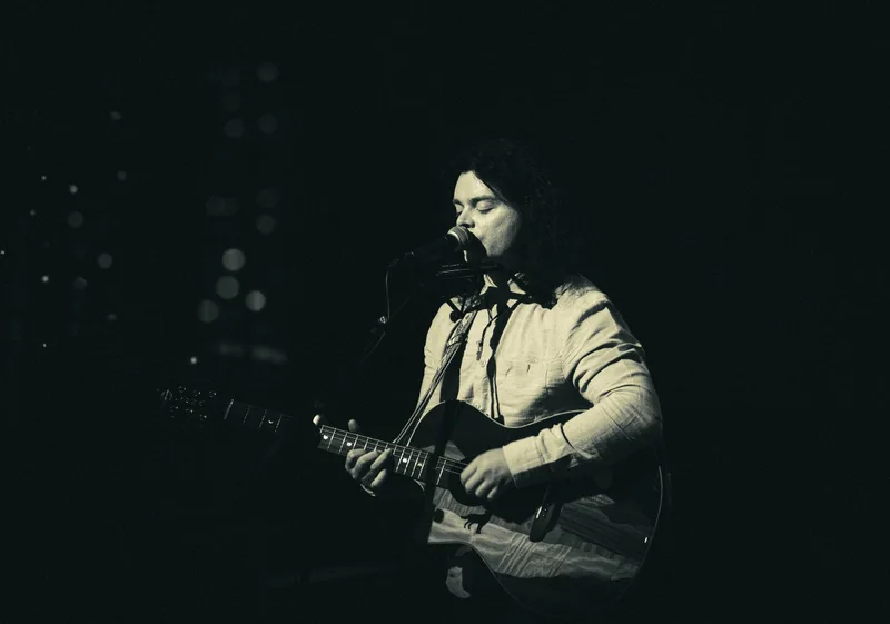Black and white shot of a long-haired singer at the microphone, eyes closed.