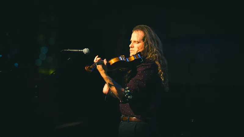 A violinist mid-phrase, the instrument catching the stage light.