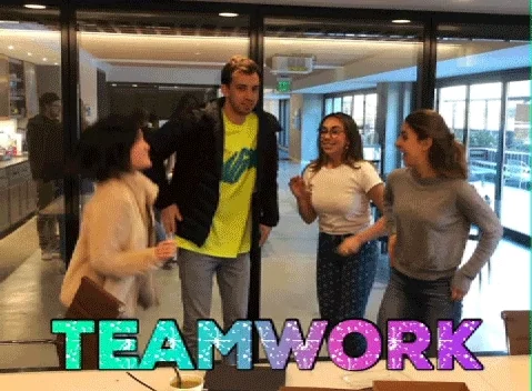 A group of people in an office jumping and doing a high five. The text reads: "Teamwork"