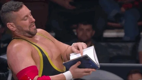 A wrestler reads a book in the ring and throws it over the ropes.