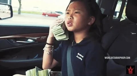 A child in a car holds up stacks of cash.