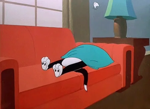 Sylvester the Cat laying with a pillow over him on a couch while a feather floats above him.