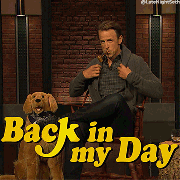 Seth Myers smoking a pipe and wearing an old sweater. He says, 'Back in my day...' as he pets a stuffed dog.