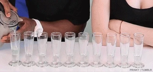 Someone pouring rainbow shots into bar glasses.