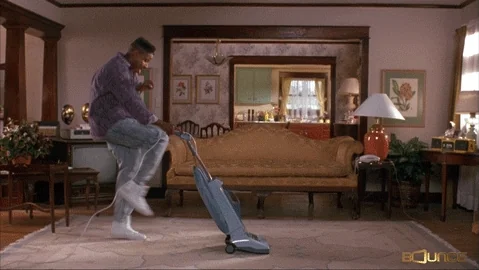 A person happily vacuuming a carpet in their house.