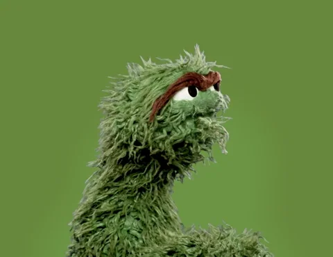 Oscar the Grouch brings his hand to his head and lets out a big sigh.