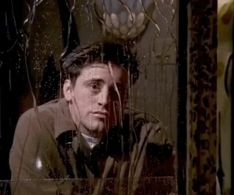 Joey from Friends looking lonely into a mirror as fake rain pours down it,