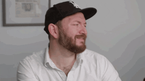 A man wearing a black baseball cap and saying, 