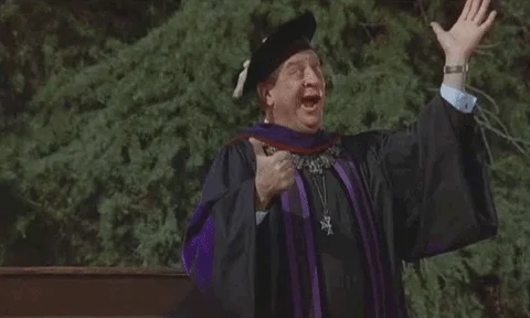 College staff member (Rodney Dangerfield) standing in the middle falling of graduation caps