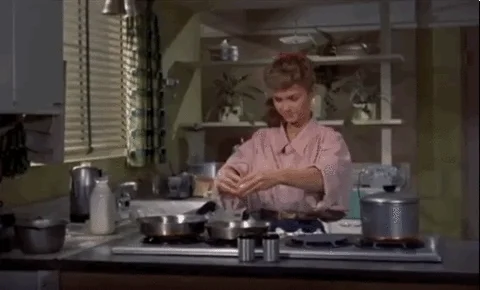 A  woman in a kitchen cracking an egg and throwing away the shell.
