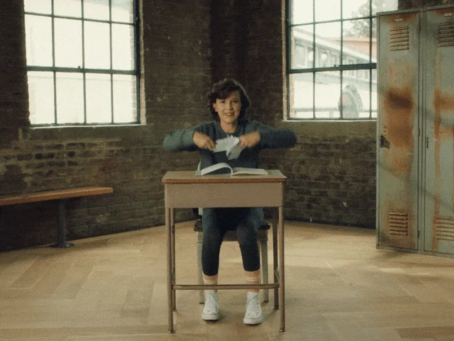 A student at a desk throws her papers in the air triumphantly.