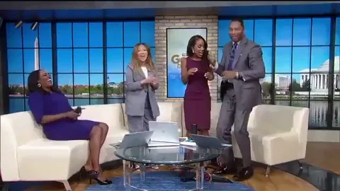 A group of people in a TV studio are dancing in front of a couch, celebrating something.