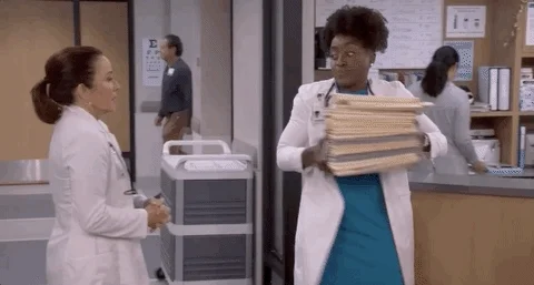 Two people wearing white lab coats, one handing a large stack of documents to the other.