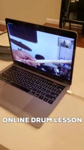 A drum teacher conducts an online drum lesson over a laptop.
