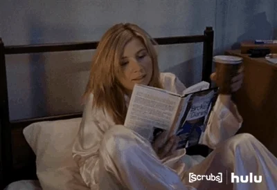 A woman in silk pajamas gets comfortable in bed with a book and a cup of tea.