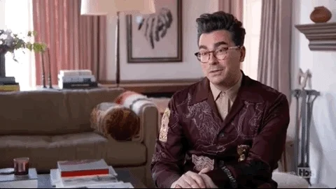 Dan Levy sitting in a living room purses his lips, says 