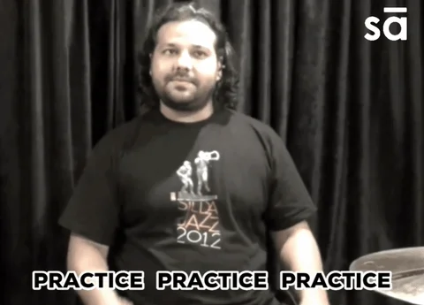 A man sitting at a drum kit making a drumming motion with his arms. The caption reads: 
