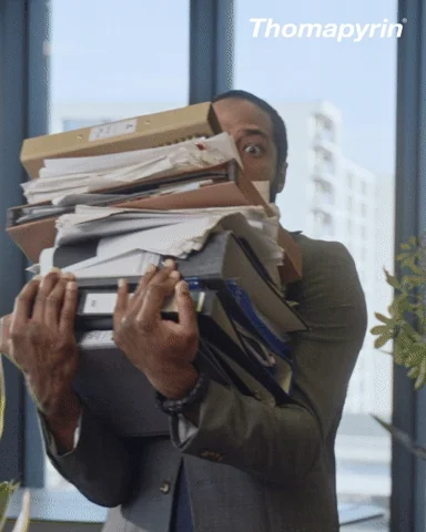 A man carrying a big stack of files and sheets at work and losing his balance.