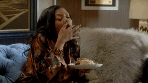 celebrity Taraji P Henson holding a plate full of food, chewing, and licking her fingers.