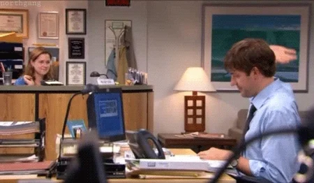 Pam and Jim from The Office give each other a high five from across their desks.
