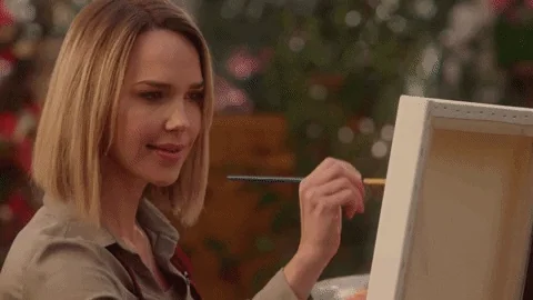 A woman happily painting on a canvas.