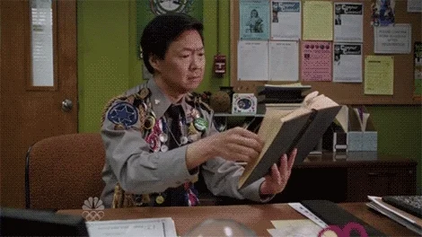 A person at an office desk reviewing a book while smiling.
