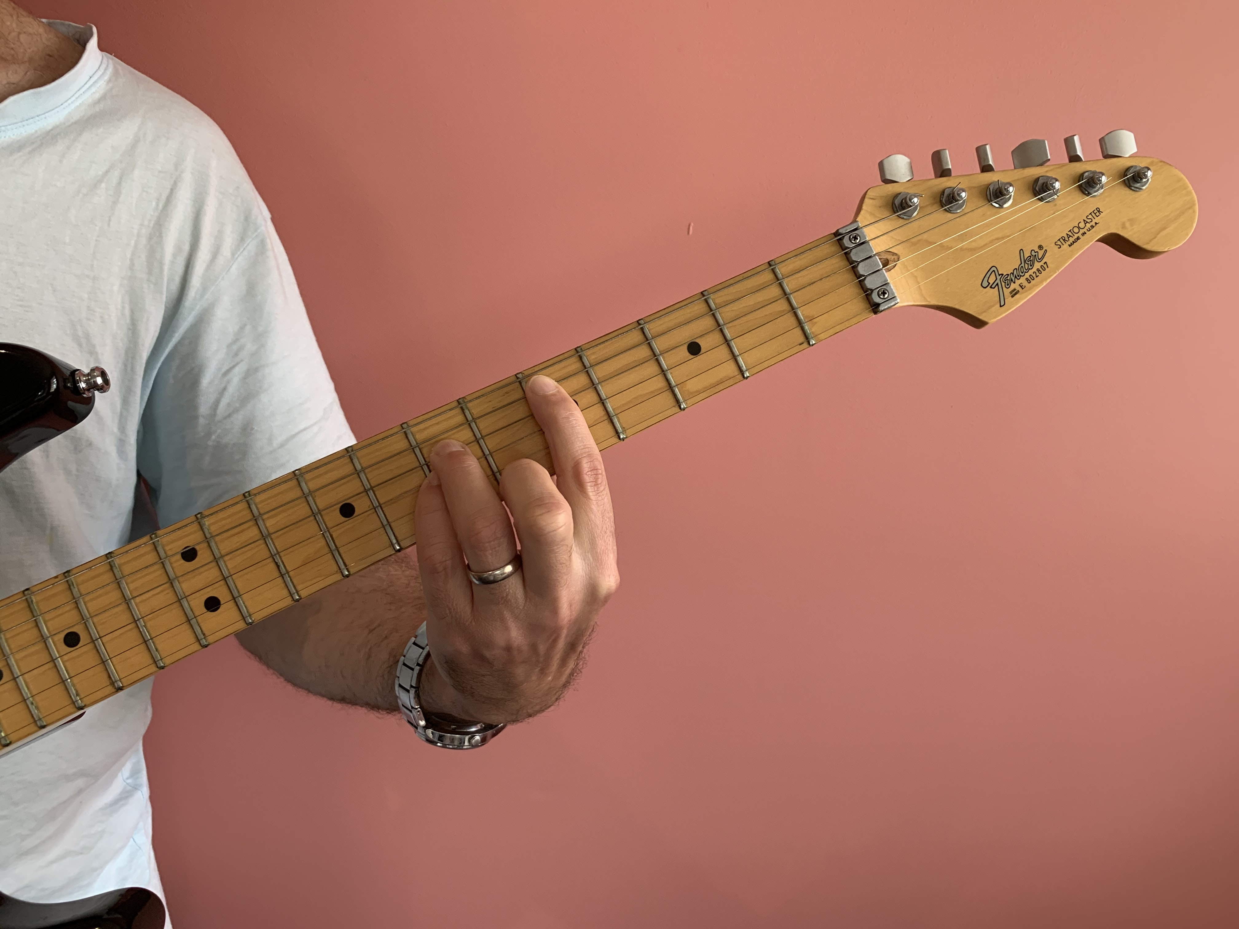 Image of person playing guitar. Their fingers are closed close to (but not on) the fret rod closest to the tone hole.