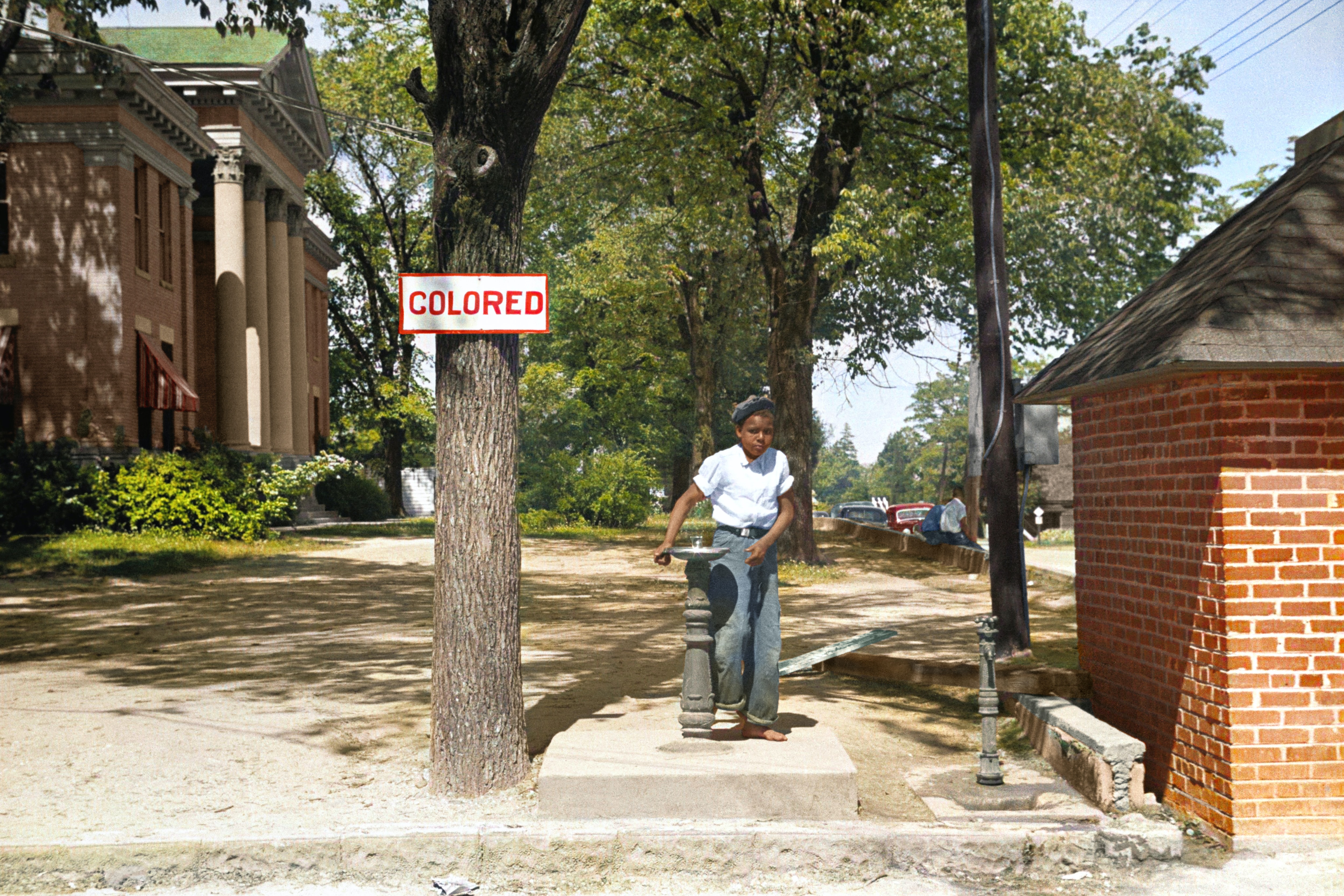 Black boy outside next to 'colored' sign on tree.