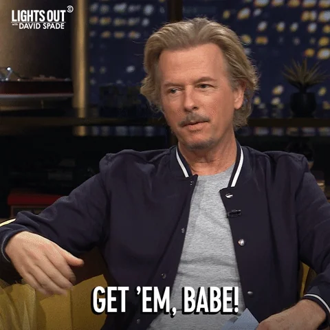 David Spade wearing a navy jacket, making a funny face. He says,