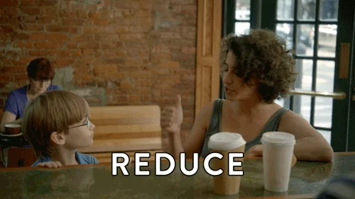 Alana from Broad city sits in a cafe with a child in front of two coffee cups. She says, 'Reduce, reuse, recycle, Rihanna!'