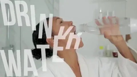 A woman in a bathrobe drinking water in the bathroom